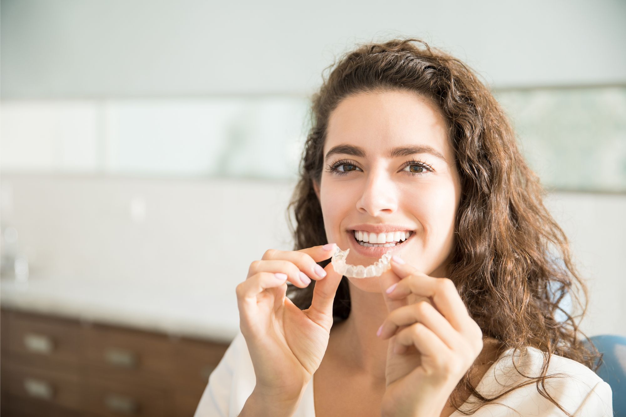 Smiling woman holding Invisalign aligner at Glendale orthodontic office
